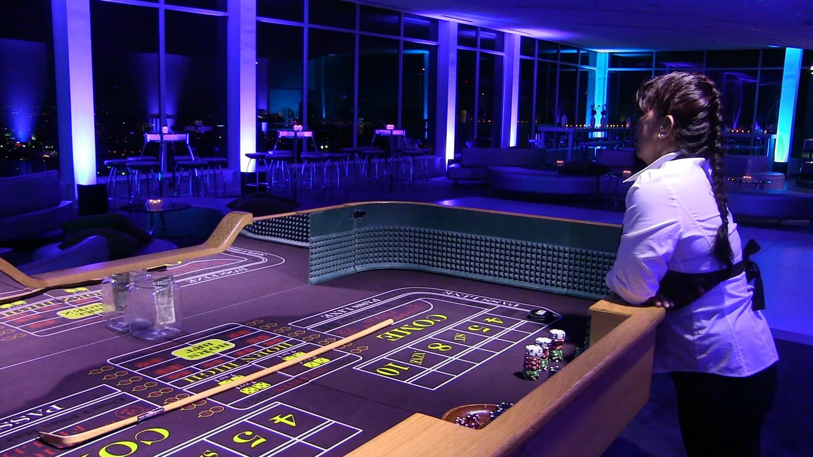 Professional dealer at a craps table during an upscale rooftop casino event with city skyline views